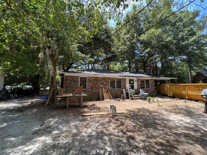 Brick ranch mid-renovation with new roof going on, dumpster and materials in the yard, Georgia.